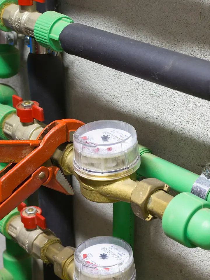 Encanador apertando com chave de grifo a conexão de um hidrômetro na tubulação verde